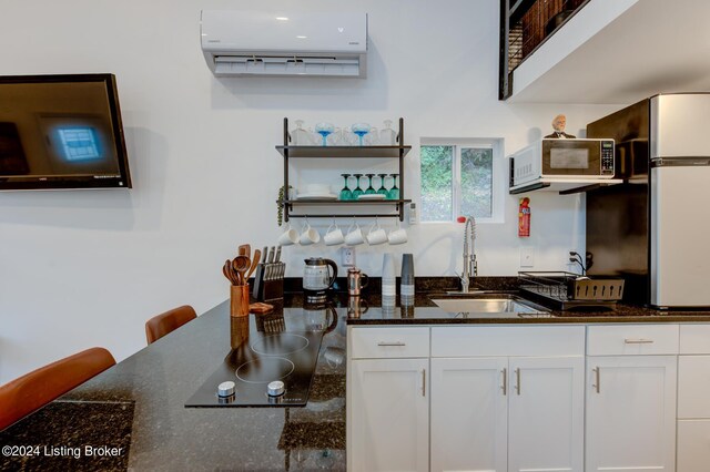 kitchen featuring white cabinets, dark stone countertops, a wall unit AC, and sink