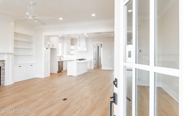 unfurnished living room featuring sink, light hardwood / wood-style flooring, ceiling fan, ornamental molding, and a brick fireplace