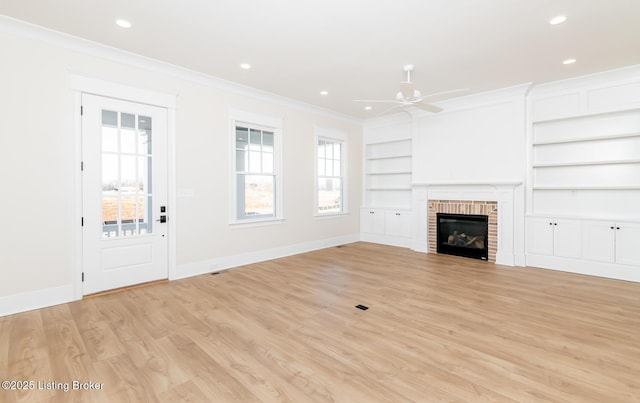 unfurnished living room with built in features, ornamental molding, ceiling fan, light hardwood / wood-style floors, and a brick fireplace