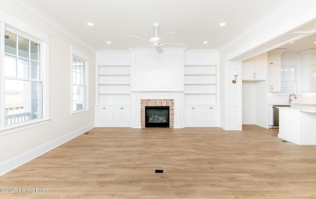 unfurnished living room featuring crown molding, light hardwood / wood-style flooring, built in features, ceiling fan, and a fireplace