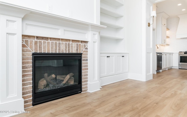 interior details featuring built in features, stainless steel stove, black dishwasher, hardwood / wood-style flooring, and a brick fireplace