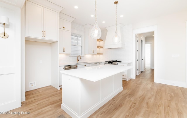 kitchen with pendant lighting, sink, white cabinetry, a center island, and light hardwood / wood-style floors