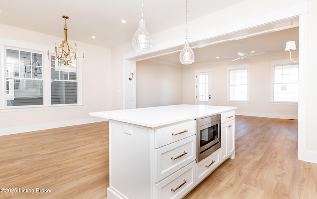 kitchen featuring stainless steel microwave, a center island, hanging light fixtures, and white cabinets