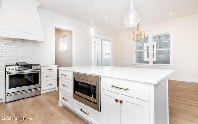 kitchen featuring premium range hood, appliances with stainless steel finishes, white cabinetry, hanging light fixtures, and a center island