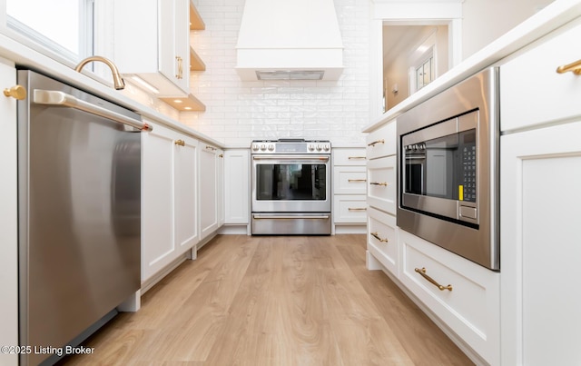 kitchen featuring custom exhaust hood, stainless steel appliances, light hardwood / wood-style floors, and white cabinets