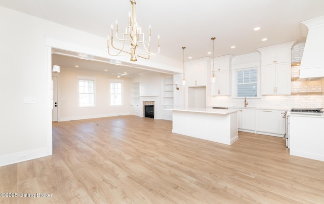 kitchen with white cabinetry, a tile fireplace, a kitchen island, pendant lighting, and light hardwood / wood-style floors