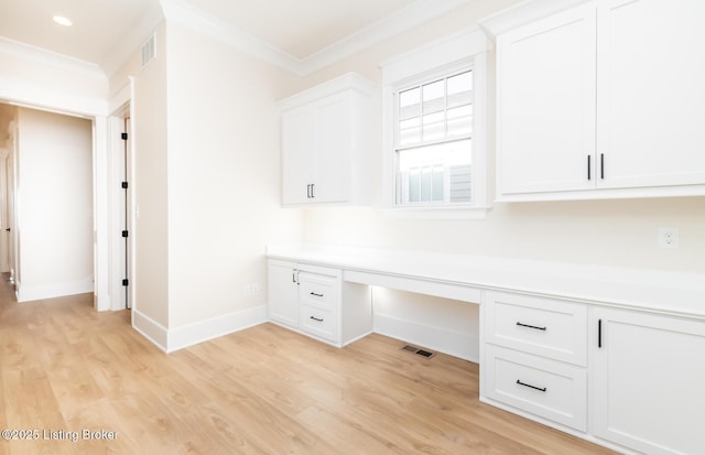 unfurnished office featuring crown molding, built in desk, and light wood-type flooring