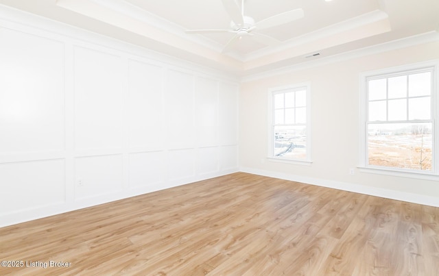 spare room featuring ornamental molding, a raised ceiling, light wood-type flooring, and a wealth of natural light