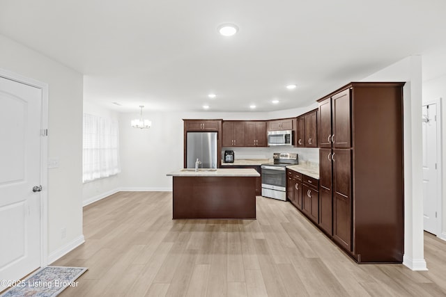 kitchen with a kitchen island with sink, hanging light fixtures, dark brown cabinets, stainless steel appliances, and light wood-type flooring