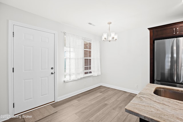 interior space featuring dark brown cabinetry, light stone counters, decorative light fixtures, stainless steel refrigerator, and light hardwood / wood-style floors