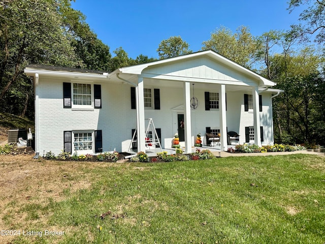 view of front of property featuring central AC unit, covered porch, and a front yard