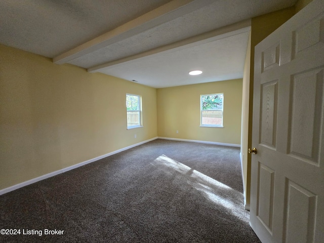 unfurnished room with carpet, a healthy amount of sunlight, beam ceiling, and a textured ceiling