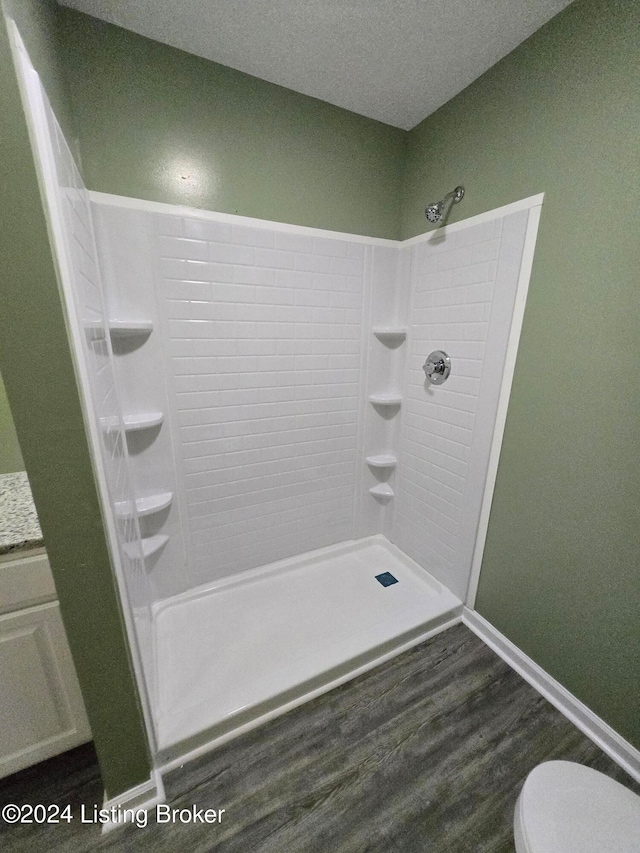 bathroom featuring toilet, wood-type flooring, a textured ceiling, and walk in shower