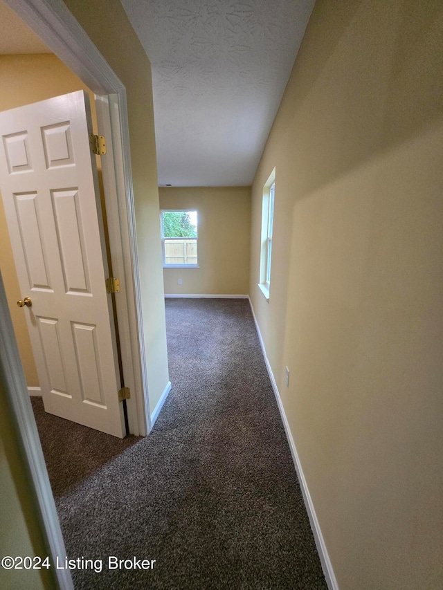 corridor featuring a textured ceiling and dark colored carpet