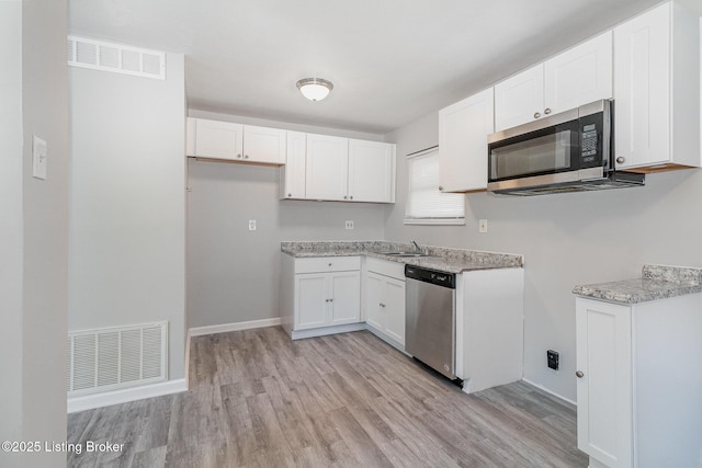 kitchen with light stone counters, stainless steel appliances, light hardwood / wood-style floors, and white cabinets