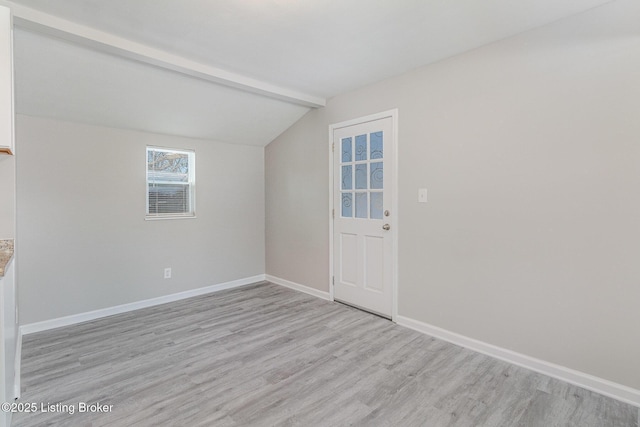 empty room featuring light wood-type flooring and lofted ceiling with beams