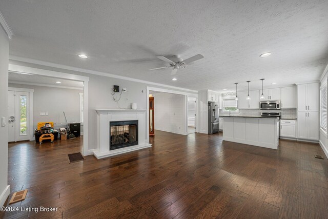 unfurnished living room with ceiling fan, a multi sided fireplace, ornamental molding, a textured ceiling, and dark wood-type flooring