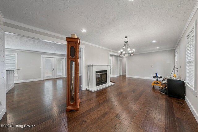 unfurnished living room with a textured ceiling, crown molding, dark wood-type flooring, and a chandelier