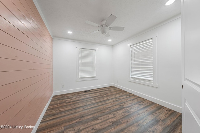 empty room with dark hardwood / wood-style flooring, a textured ceiling, wood walls, crown molding, and ceiling fan