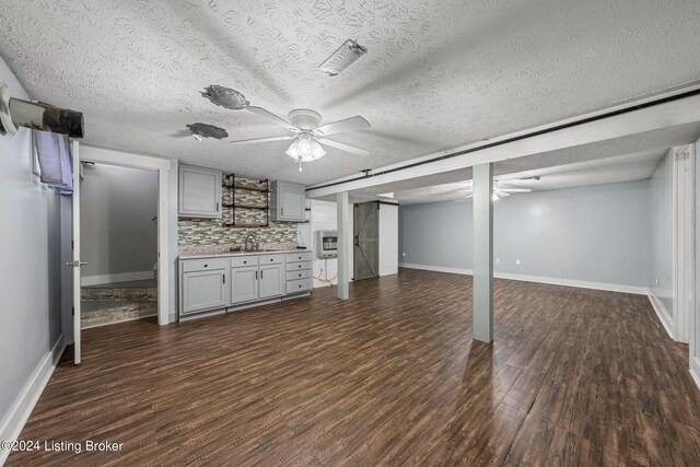 unfurnished living room featuring ceiling fan, a textured ceiling, dark hardwood / wood-style floors, and sink