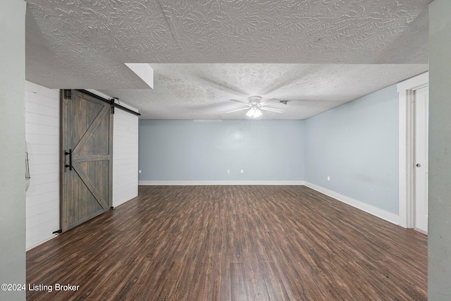 basement featuring ceiling fan, a textured ceiling, dark wood-type flooring, and a barn door