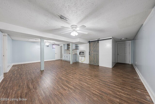 basement with a textured ceiling, a barn door, and dark hardwood / wood-style flooring