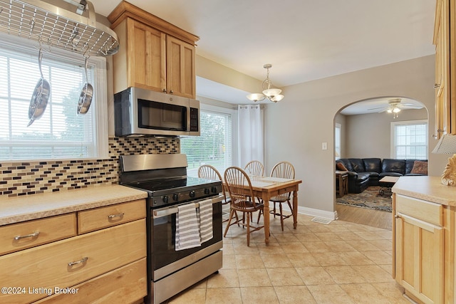 kitchen with tasteful backsplash, ceiling fan with notable chandelier, stainless steel appliances, decorative light fixtures, and light tile patterned floors