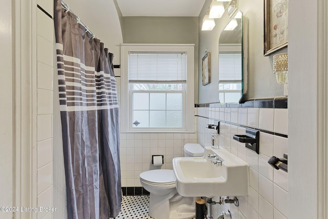 bathroom with tile walls, tile patterned flooring, a shower with shower curtain, toilet, and sink