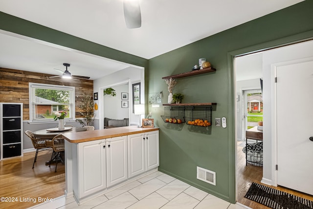 kitchen featuring light hardwood / wood-style floors, white cabinets, kitchen peninsula, wooden walls, and ceiling fan