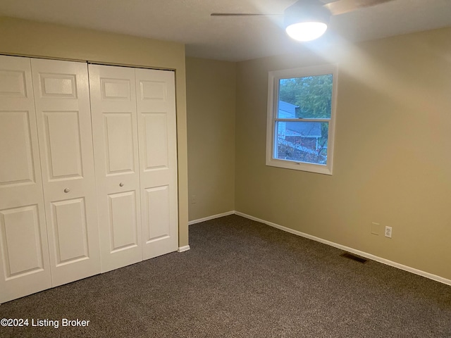 unfurnished bedroom with dark colored carpet, ceiling fan, and a closet