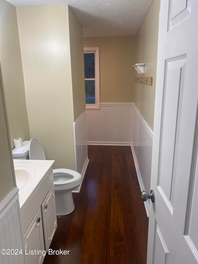 bathroom with wood-type flooring, vanity, toilet, and a textured ceiling