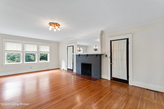 unfurnished living room with a brick fireplace, a chandelier, hardwood / wood-style flooring, and crown molding