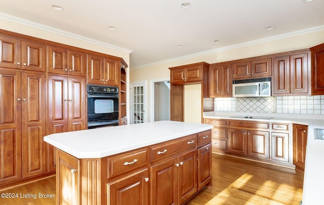 kitchen featuring a center island, hardwood / wood-style flooring, decorative backsplash, black appliances, and ornamental molding