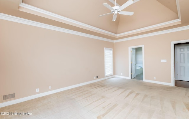 empty room with ceiling fan, ornamental molding, a tray ceiling, light colored carpet, and a towering ceiling