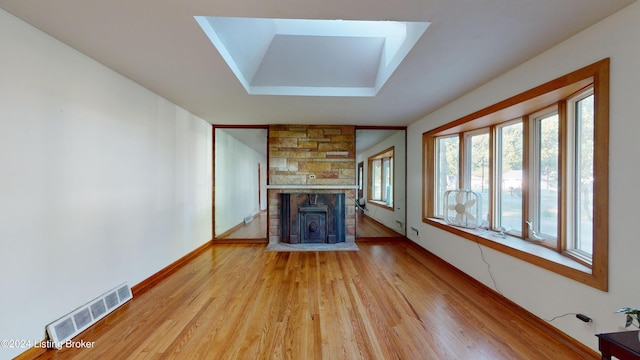 unfurnished living room featuring a stone fireplace, wood-type flooring, a tray ceiling, and a skylight