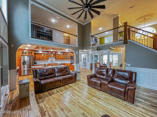 living room featuring ceiling fan with notable chandelier, light wood-type flooring, ornamental molding, and a high ceiling