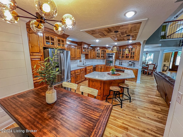 dining area featuring sink, a textured ceiling, light hardwood / wood-style flooring, wooden walls, and ornate columns