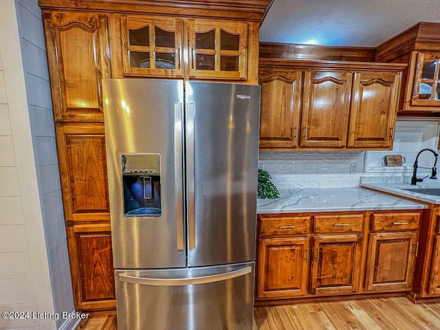 kitchen featuring tasteful backsplash, stainless steel fridge with ice dispenser, light stone counters, and light hardwood / wood-style flooring