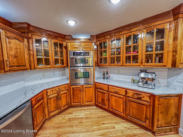 kitchen with a textured ceiling, decorative backsplash, light hardwood / wood-style flooring, and stainless steel appliances