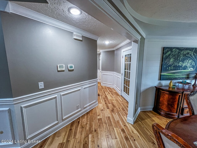 corridor featuring a textured ceiling, crown molding, and light hardwood / wood-style floors