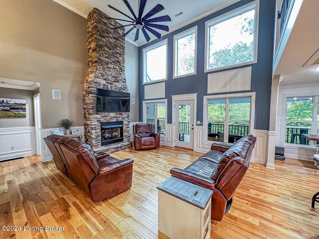 living room featuring light hardwood / wood-style floors, ornamental molding, a towering ceiling, and a fireplace