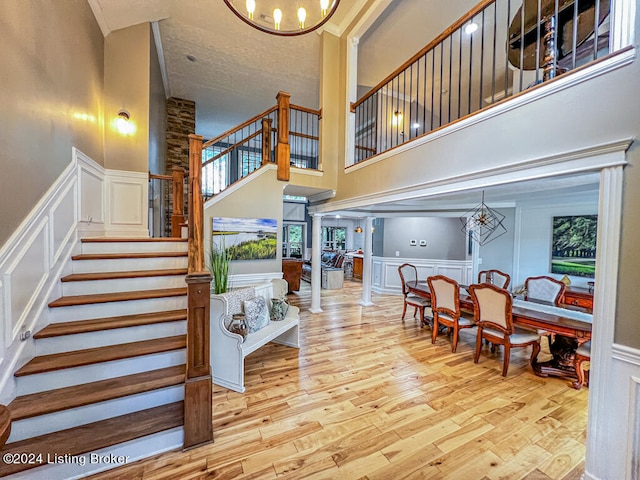 stairway featuring wood-type flooring, a chandelier, a wealth of natural light, a towering ceiling, and ornate columns