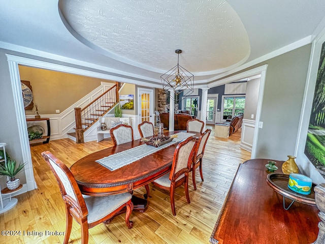 dining area with a textured ceiling, light hardwood / wood-style floors, an inviting chandelier, ornamental molding, and ornate columns