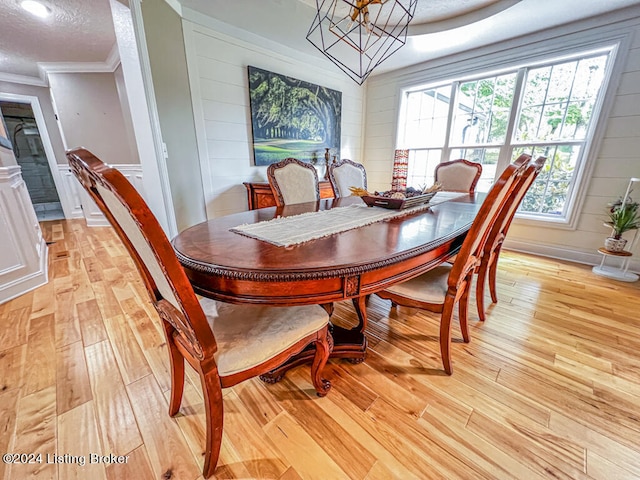 dining space with a notable chandelier, a textured ceiling, light hardwood / wood-style floors, and crown molding