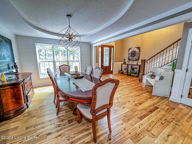 dining space featuring light wood-type flooring, a textured ceiling, a tray ceiling, and a chandelier