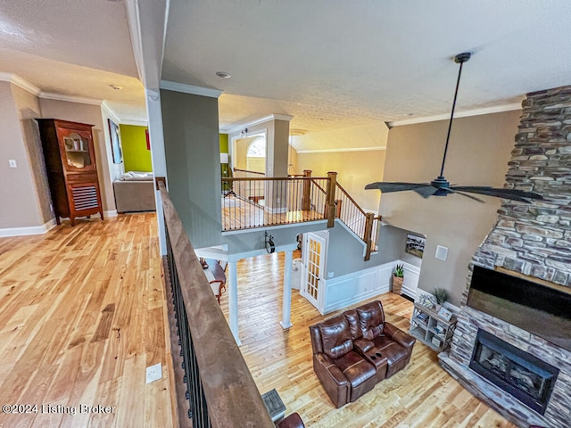 living room with a stone fireplace, ornamental molding, hardwood / wood-style floors, and ceiling fan