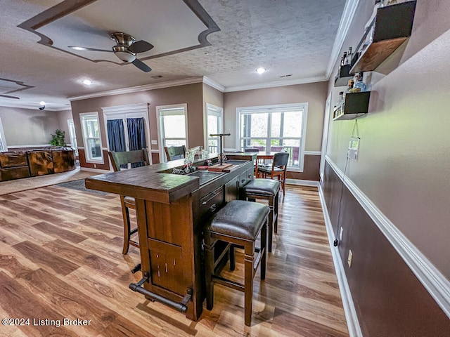 kitchen featuring wood-type flooring, a textured ceiling, a kitchen bar, ornamental molding, and ceiling fan