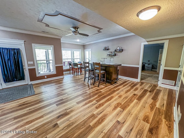 kitchen with a breakfast bar area, a textured ceiling, ceiling fan, ornamental molding, and hardwood / wood-style floors