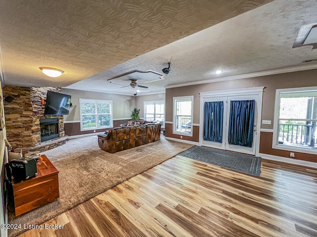 unfurnished living room with ceiling fan, ornamental molding, a stone fireplace, a textured ceiling, and hardwood / wood-style floors