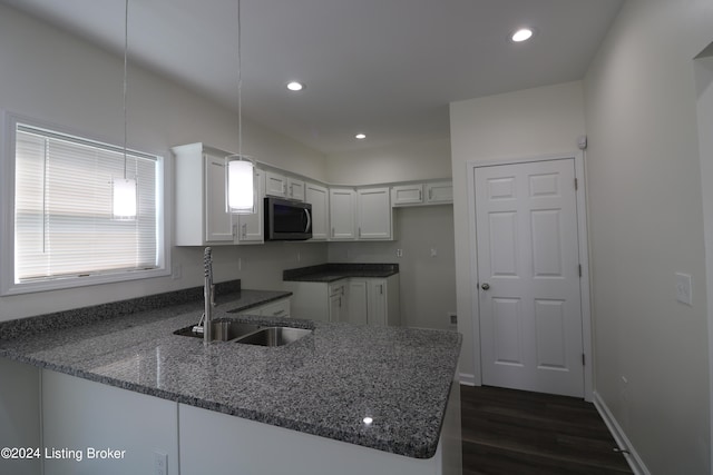 kitchen featuring dark hardwood / wood-style floors, white cabinets, kitchen peninsula, decorative light fixtures, and dark stone countertops